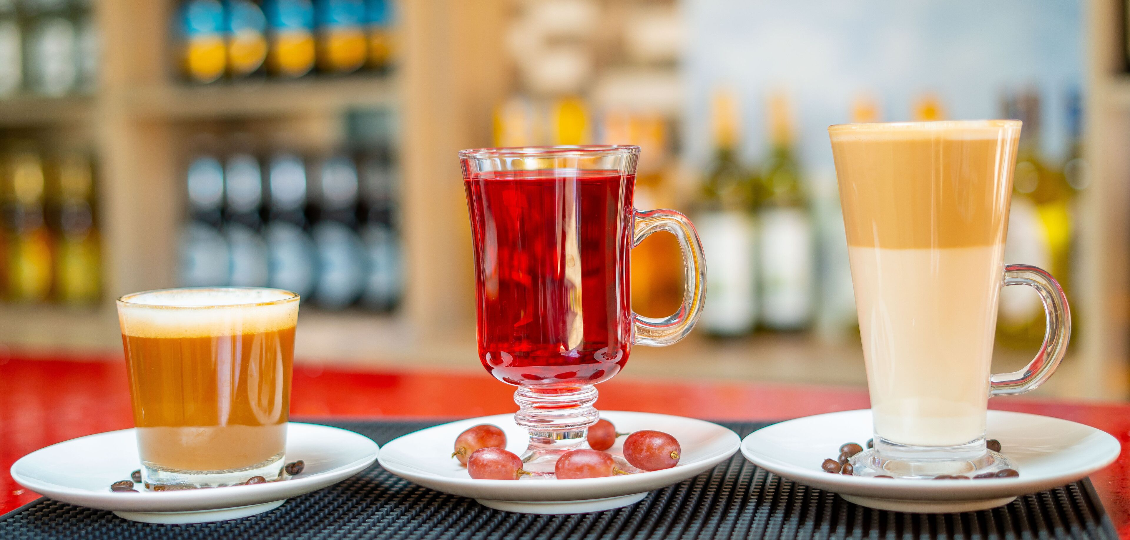 Three glasses of beverages on white saucers with coffee beans.