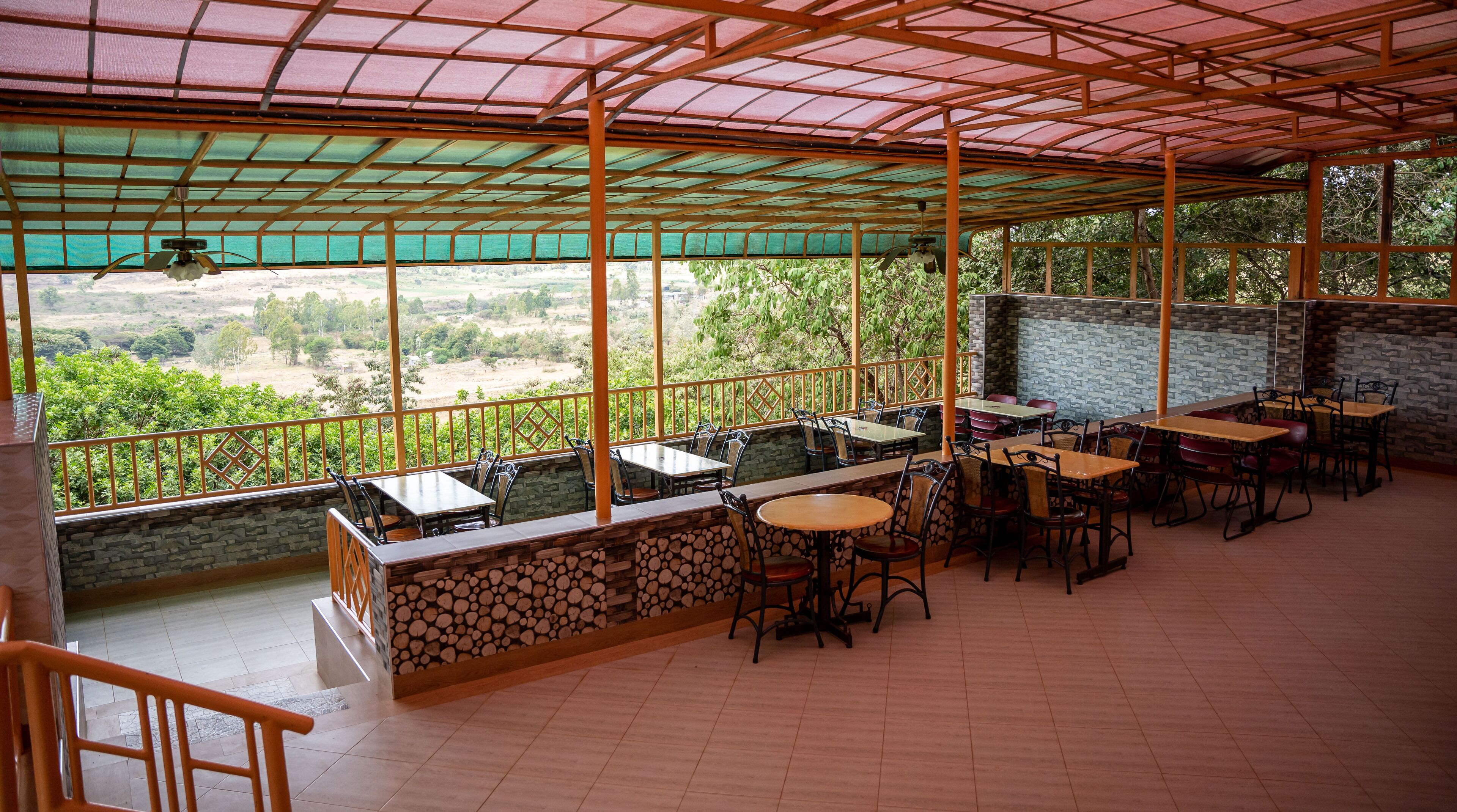 Un espacio al aire libre cubierto para comer, con mesas y sillas, un muro de piedra y vistas al campo.