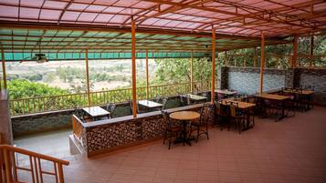 Un espacio al aire libre cubierto para comer, con mesas y sillas, un muro de piedra y vistas al campo.