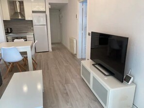 A modern kitchen with white appliances, a dining area with a white table and chairs, and a flat-screen TV on a white stand.