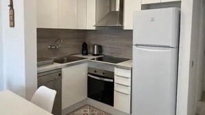 Eine moderne Küche mit weißen Schränken, einer Edelstahl-Spüle, einem eingebauten Backofen und einem weißen Kühlschrank.