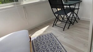 Ein kleines Zimmer mit Fenster, Schreibtisch mit Stuhl und einem gemusterten Teppich.