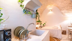 Eine kleine Küche mit Spüle, Geschirrgestell und Mikrowelle. Ein Bett mit weißer Bettdecke und ein kleiner Nachttisch sind ebenfalls vorhanden.