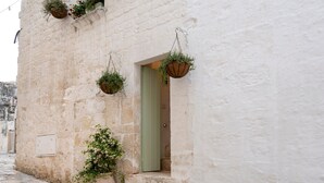 Eine enge Pflasterstraße mit einem weißen Gebäude, einer grünen Tür und hängenden Blumenkästen.
