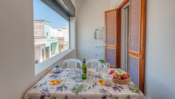 Un balcon avec une table dressée pour le dîner, une bouteille, une carafe et un panier de fruits.