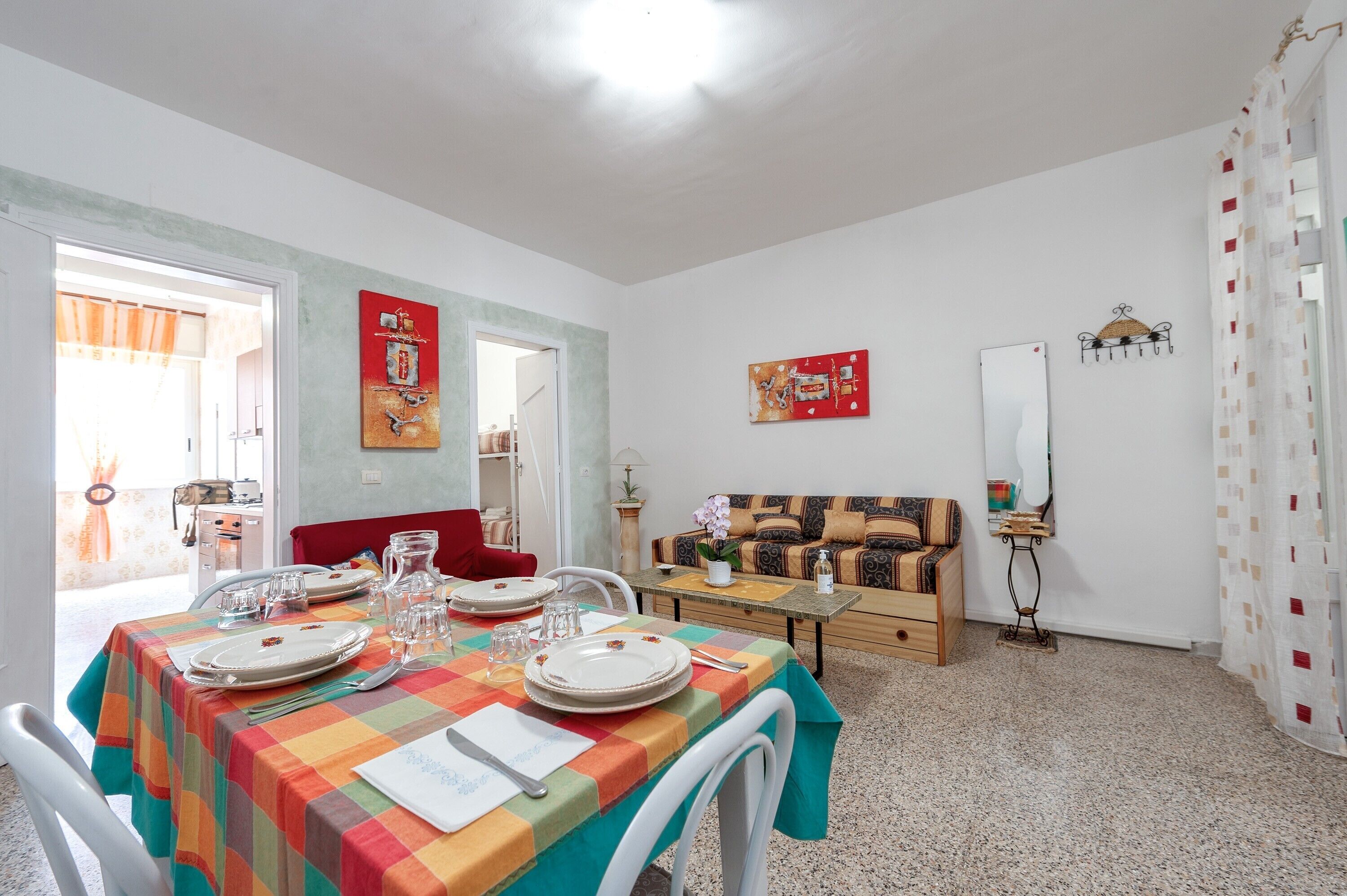 A dining area with a table set for four, a sofa, and a mirror on the wall.