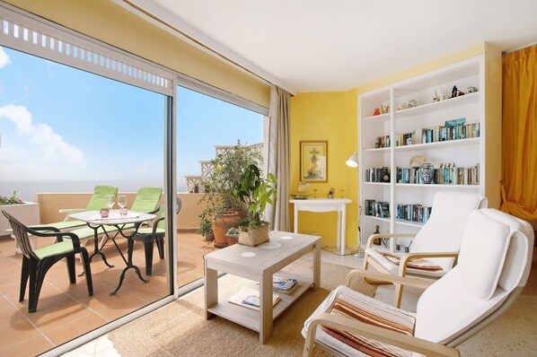 Un espace de vie avec un balcon, une bibliothèque et une table avec des chaises.