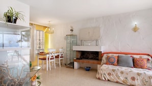 Una sala de estar con sofá, una mesa de vidrio, chimenea y comedor.