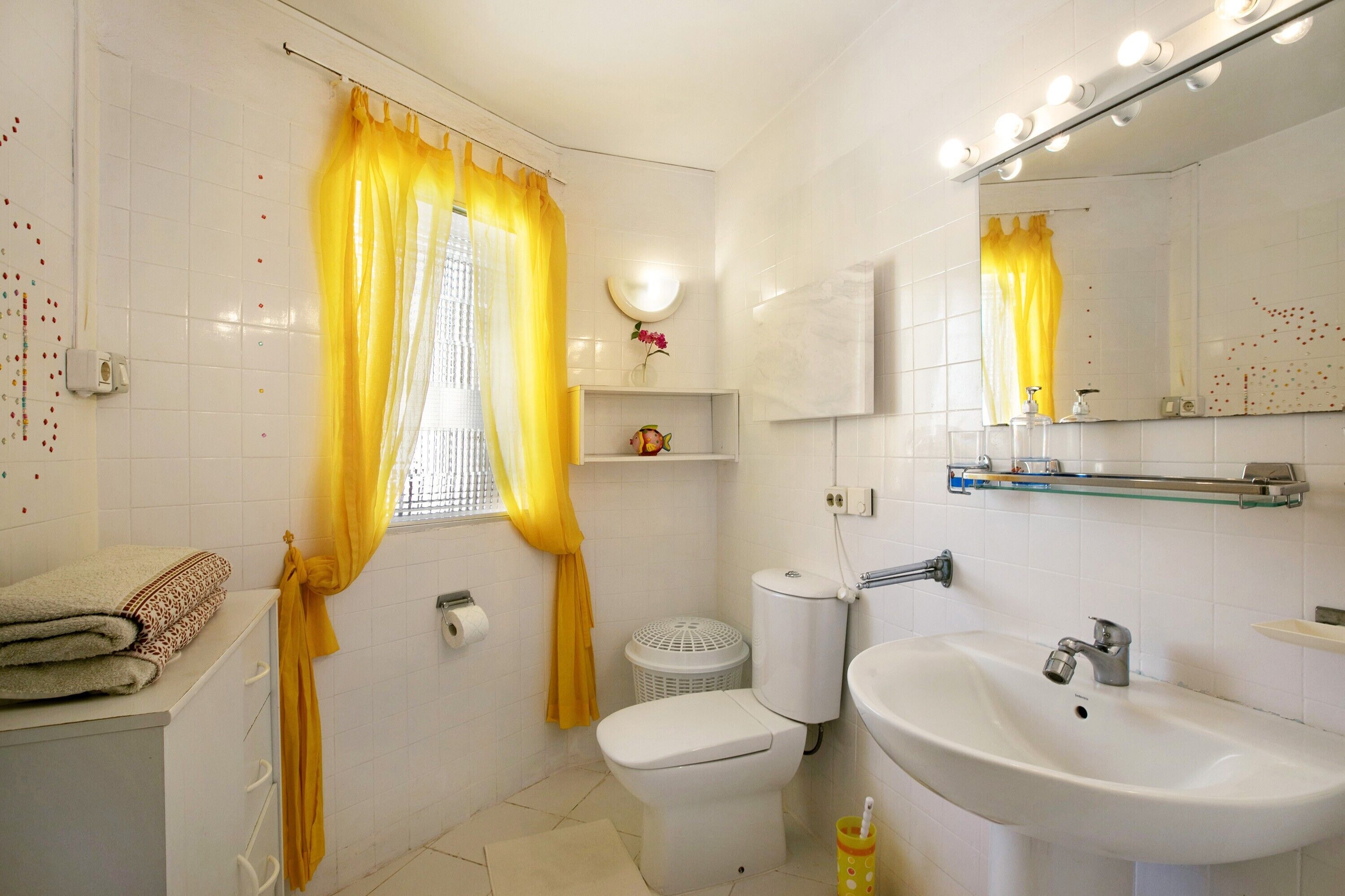 Un baño con inodoro, lavamanos, espejo y cortinas amarillas.