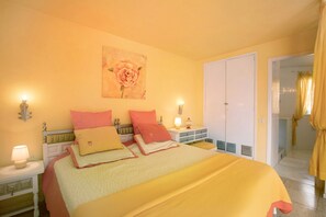 Une chambre à coucher comprenant un lit, des tables de chevet, une lampe fixée au mur, une porte et une fenêtre avec des rideaux.