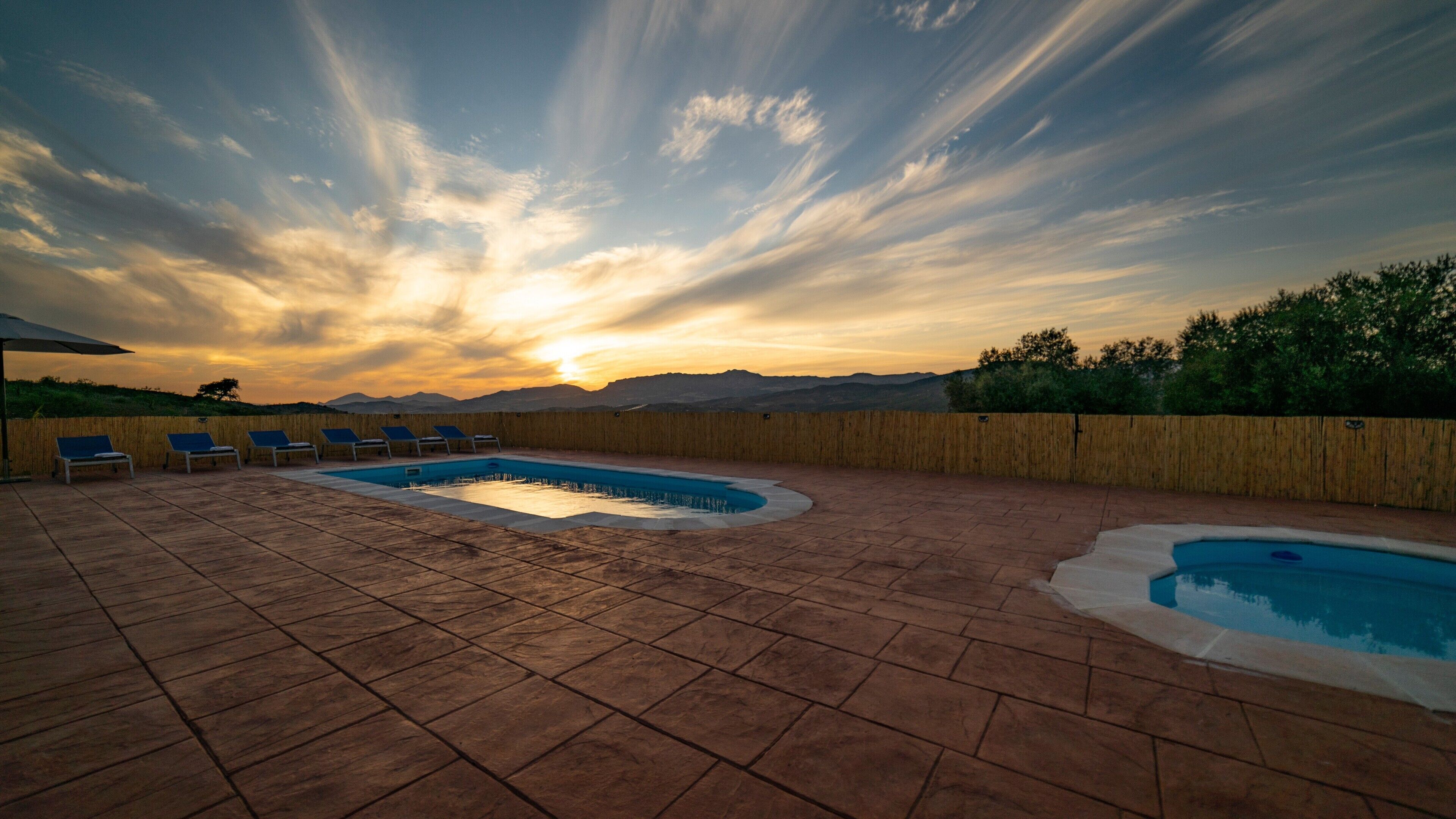 A rooftop pool with lounge chairs and a view of the sunset.