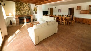 Un amplio salón con chimenea de piedra, un sofá, una mesa de comedor de madera y sillas.