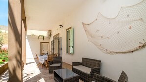 A sunlit patio with wicker furniture, a glass table, and a netted wall decoration. - Holiday Home 'Maison Chloe' close to the Beach with Terrace, Garden & Wi-Fi (La Maddalena)