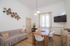 Un salon comprenant un canapé, une table à manger, des chaises, un téléviseur et un élément décoratif mural.