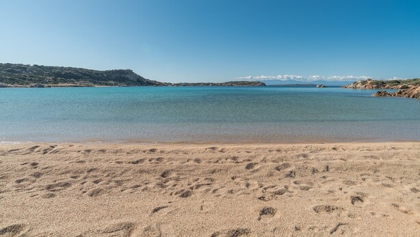 A beach with clear water, sandy shore, and distant hills. - Holiday Home 'Maison Chloe' close to the Beach with Terrace, Garden & Wi-Fi (La Maddalena)