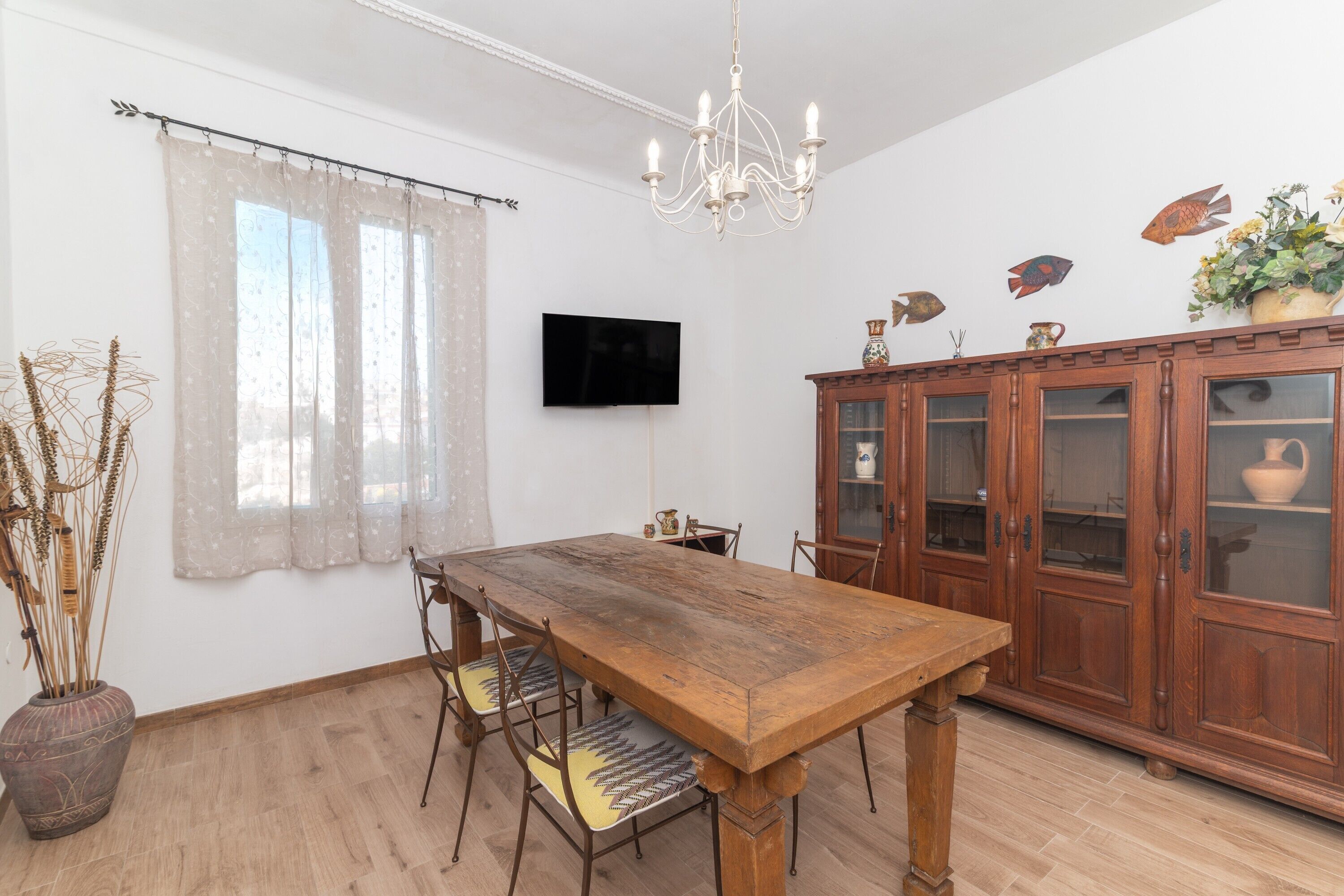 Een eetgedeelte met een houten tafel, stoelen, een kroonluchter, een televisie en een kast met glazen deuren.