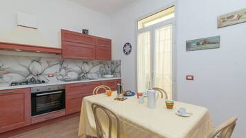 Una cucina con tavolo e sedie, piano cottura, forno e una finestra con tende.