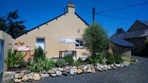 A house with a stone exterior, a gravel driveway, and a garden with various plants and a white umbrella. - Cottage 'Gîte Des Huttes' with Private Terrace, Private Garden and Wi-Fi (Bain-de-Bretagne)