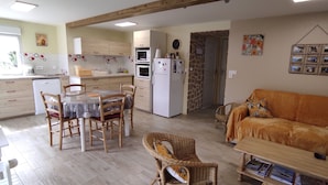 A kitchen with wooden cabinets, a dining table with chairs, a sofa, and a wall-mounted picture frame. - Cottage 'Gîte Des Huttes' with Private Terrace, Private Garden and Wi-Fi (Bain-de-Bretagne)