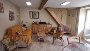 A cozy living room with a sofa, chairs, a wooden cabinet, a table, and a staircase. - Cottage 'Gîte Des Huttes' with Private Terrace, Private Garden and Wi-Fi (Bain-de-Bretagne)