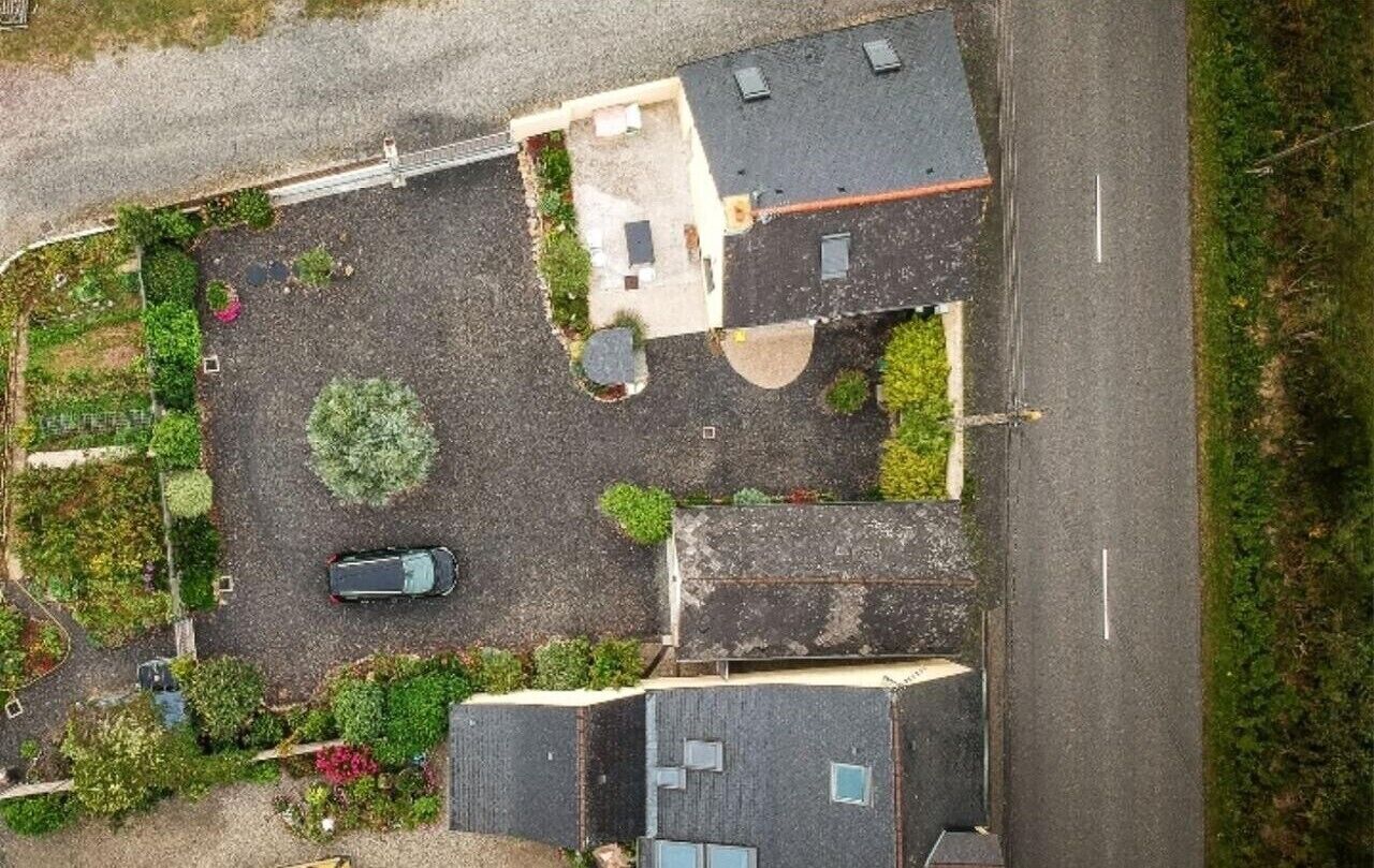 An aerial view of a residential area with a paved driveway, a parked car, and a house with a sloped roof.
