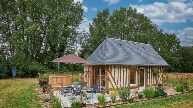 A small wooden cabin with a sloped roof, a patio with chairs, and a wooden deck.