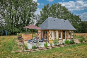 A small wooden cabin with a sloped roof, a patio with chairs, and a wooden deck.