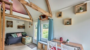 A cozy room with a wooden ceiling, a sofa, a dining table, and a window with curtains.