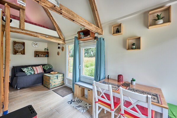 A cozy room with a wooden ceiling, a sofa, a dining table, and a window with curtains.