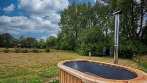 A hot tub in a wooden structure with a metal frame, surrounded by a grassy area and trees.
