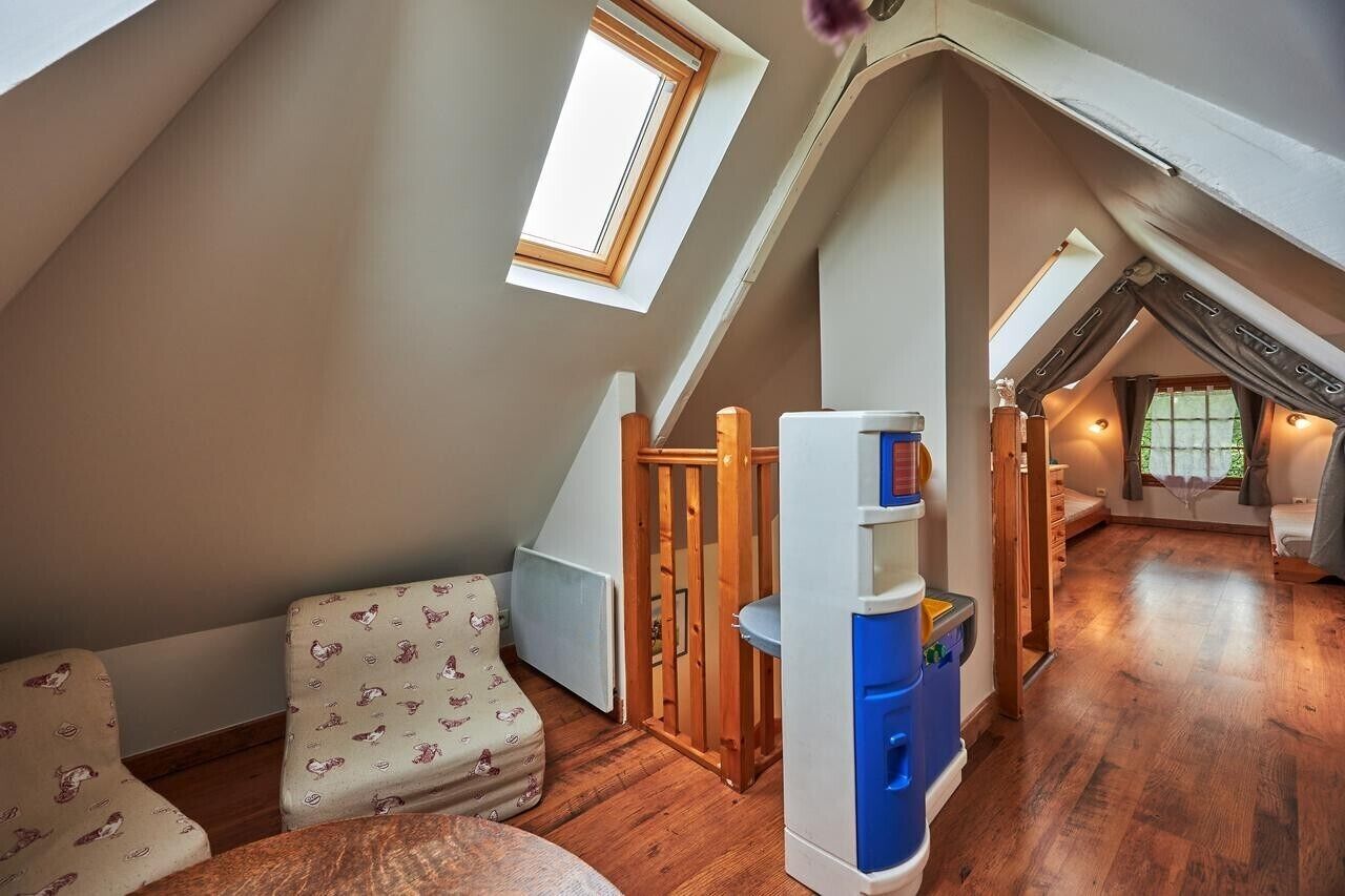 A cozy attic bedroom with a sloped ceiling, a small window, a wooden ladder, and a built-in bookshelf.