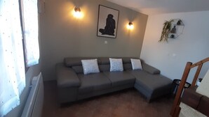 A living room with a grey sectional sofa, a wall-mounted artwork, and a small plant.