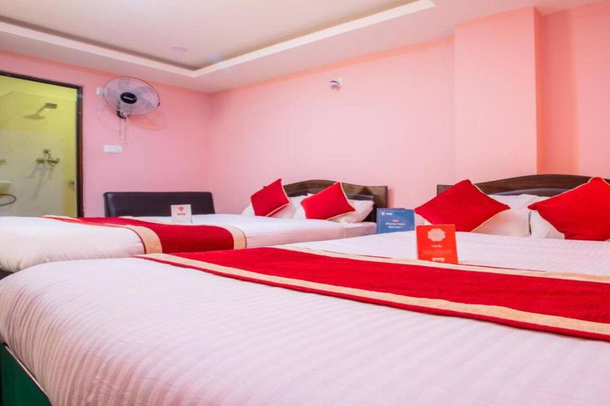 A hotel room with two beds, each with red and white bedding, and a single bed with a red blanket.