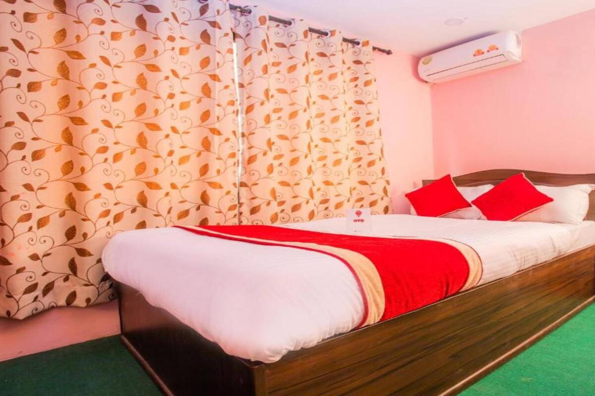 A bedroom with a bed, curtains, an air conditioner, a nightstand, and a sign.
