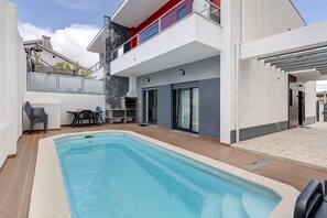 A modern poolside area with a swimming pool, outdoor seating, and a two-story building with balconies. - Holiday Home 'Sunset' with Private Pool, Wi-Fi and Air Conditioning (Fernão Ferro)