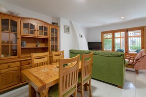 A dining area with a wooden table and chairs, a green sofa, and a television. - Holiday Home 'Casa en la Playa con Piscinas V' with Shared Pool and Air Conditioning (el Gran Alacant)