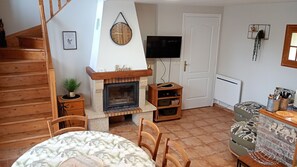 Une pièce chaleureuse avec une cheminée, un escalier en bois, un téléviseur à écran plat et une nappe à motifs.