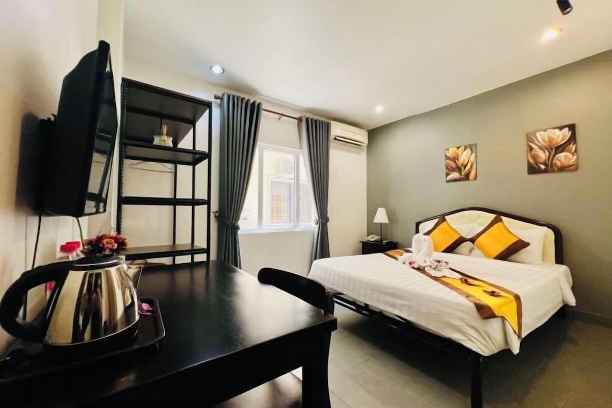 A hotel room with a bed, a desk, a chair, a television, and a window with curtains.