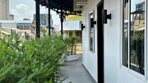 A covered outdoor area with a concrete floor, potted plants, and a building with large windows. - Sun Chakra Boutique Hotel (Phnom Penh)