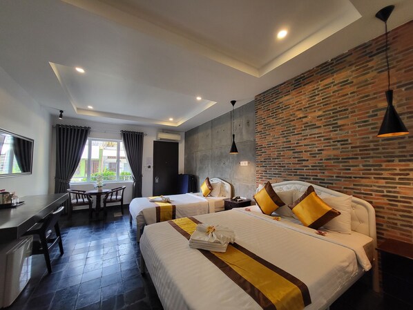 Two single beds with white bedding and brown accents, a desk, chair, and dining table, set against a backdrop of a brick-patterned wall.