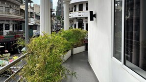 A narrow outdoor corridor with white columns, a planter with greenery, and a view of the cityscape including buildings and a restaurant. - Sun Chakra Boutique Hotel (Phnom Penh)