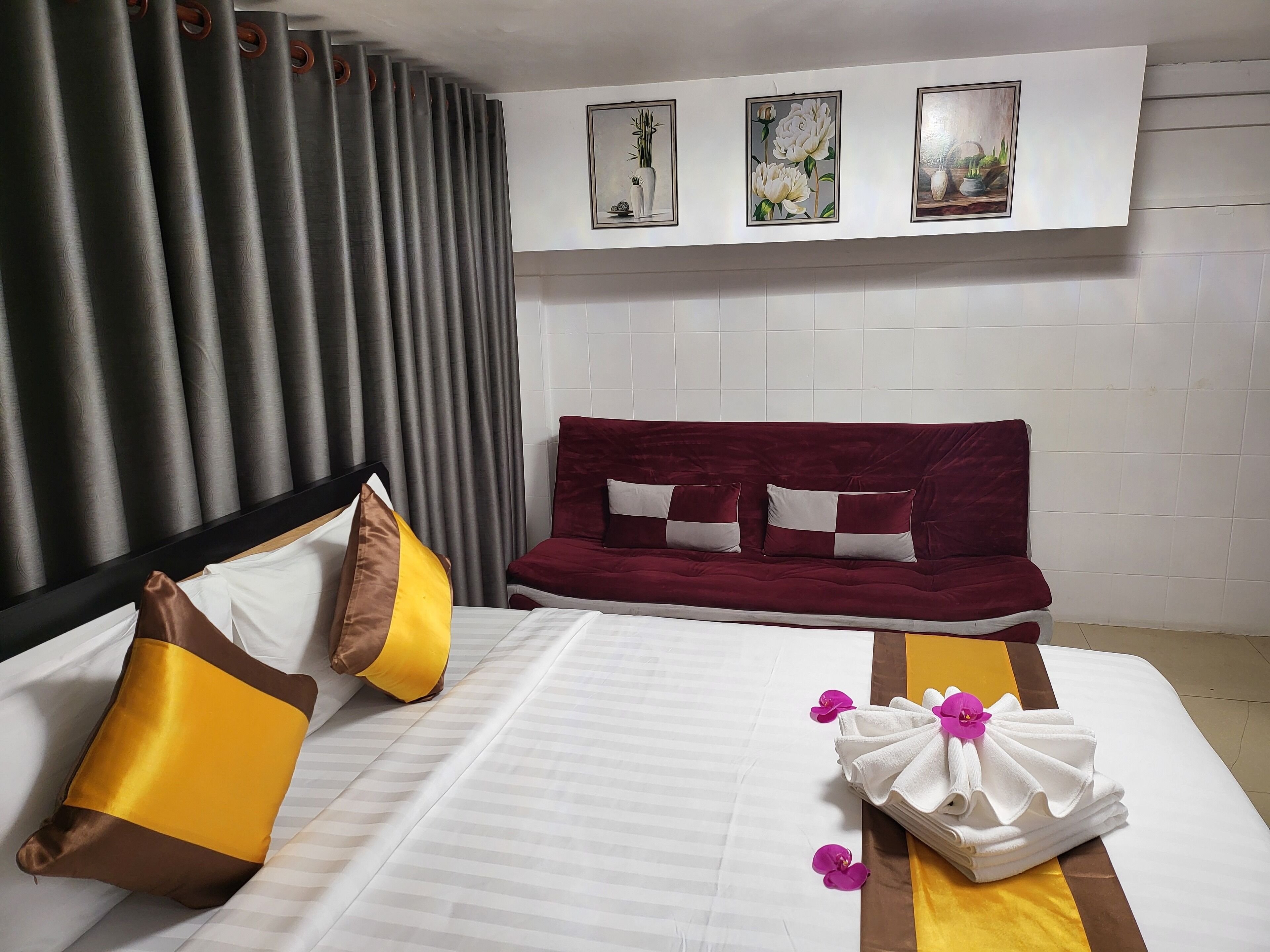 A hotel room with a bed, a red sofa, and three framed artworks on the wall.