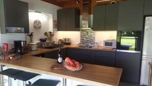 A modern kitchen with a wooden island, bar stools, and a view of the outdoors. - Maison en Bois sur Grand Jardin et à 5 Minutes de la Plage (Plobannalec-Lesconil)