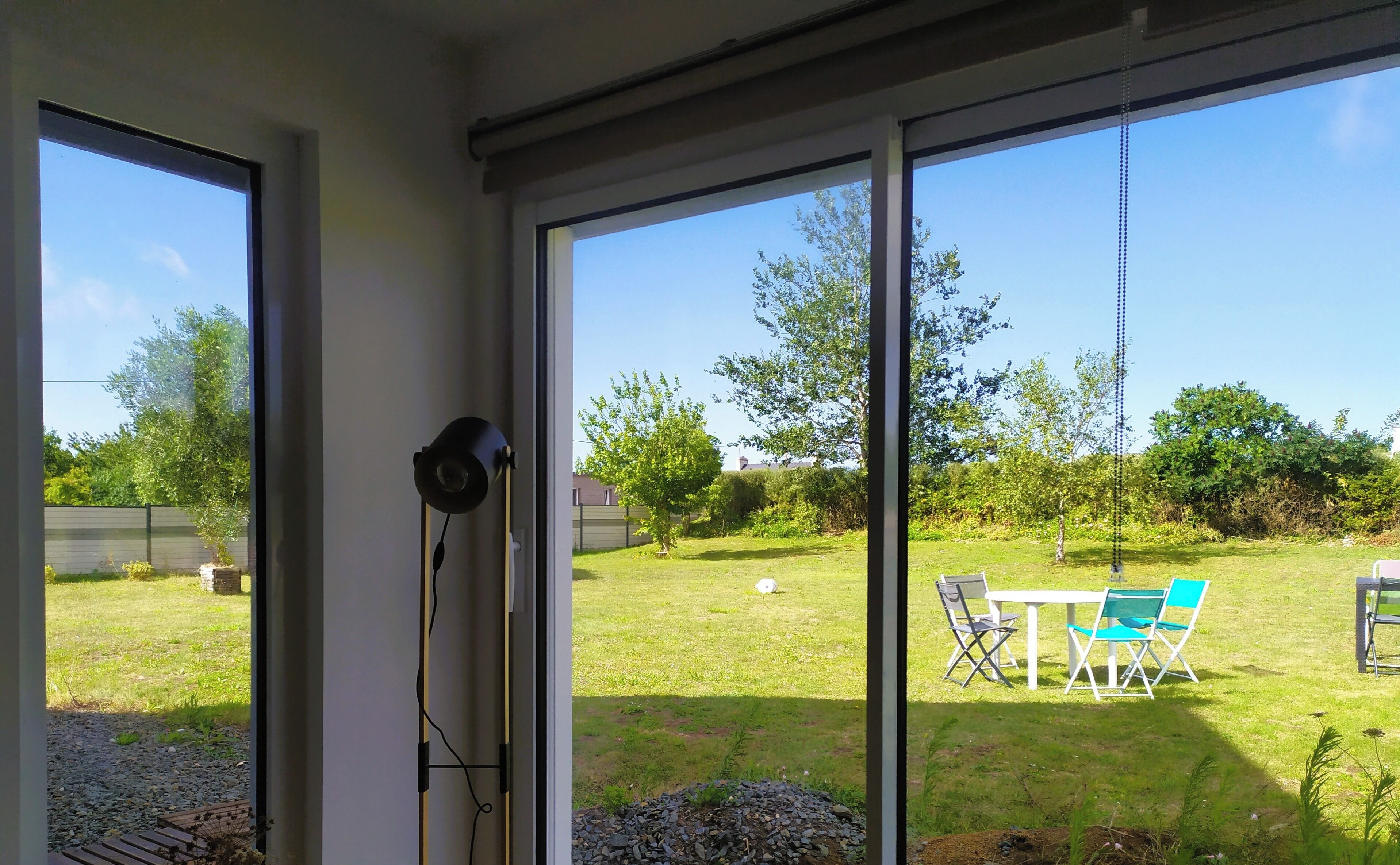 Une pièce dotée de grandes portes-fenêtres coulissantes donnant sur un jardin arrière avec une pelouse, une table et des chaises, ainsi qu’un espace aménagé en jardin.