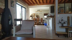 A cozy living room with a wooden ceiling, a sofa, a coffee table, and a dining area in the background. - Maison en Bois sur Grand Jardin et à 5 Minutes de la Plage (Plobannalec-Lesconil)