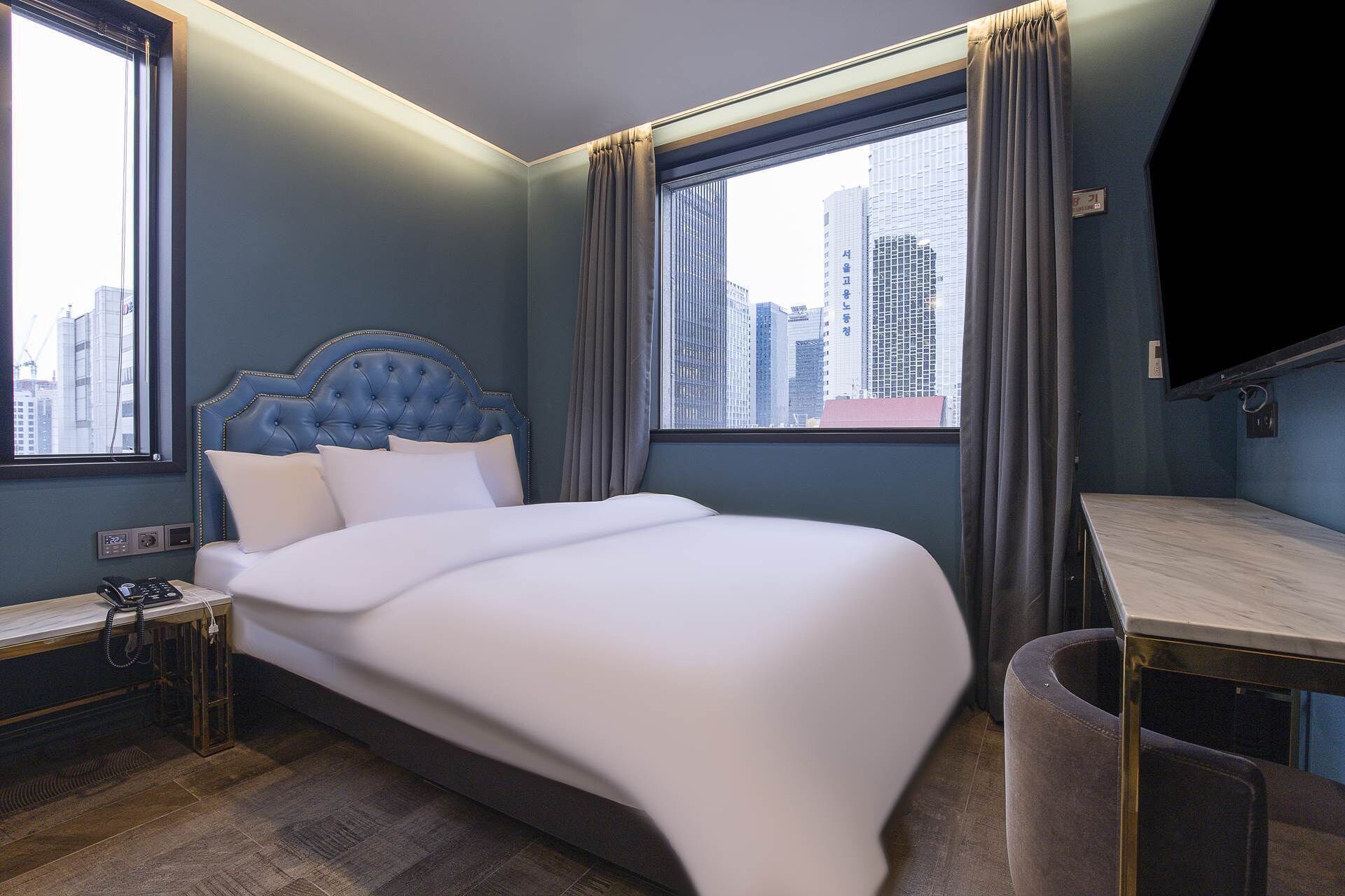 A hotel room with a large bed, a desk, and a view of the cityscape.