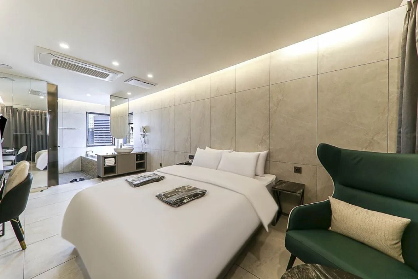 A modern hotel room with a large bed, a desk, a chair, and a green armchair.