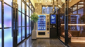 Un vestíbulo de hotel con un quiosco de auto-registro, una máquina expendedora y una planta en maceta.