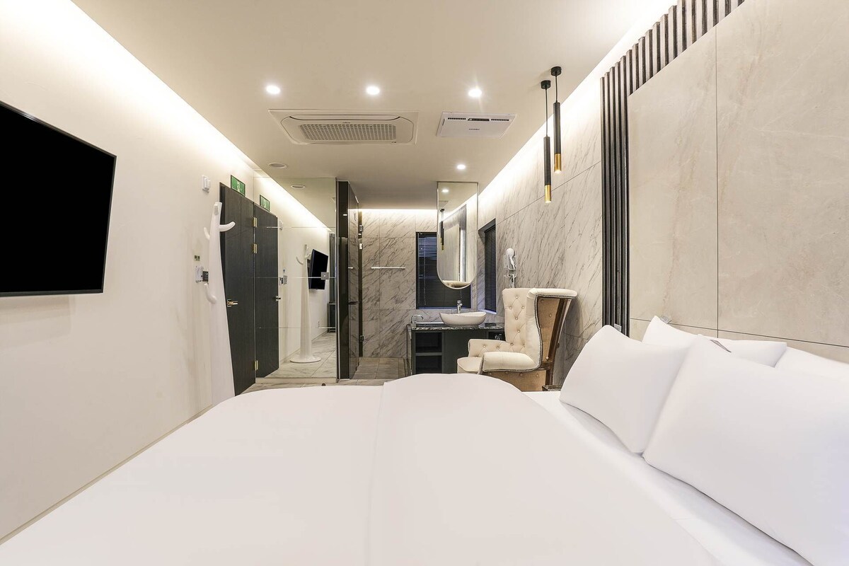 A modern hotel room with a large bed, a vanity with a mirror, and a television mounted on the wall.