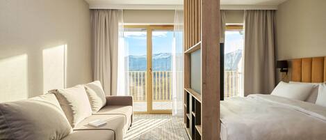 A hotel room with a bed, a sofa, a TV, and a balcony with a mountain view.
